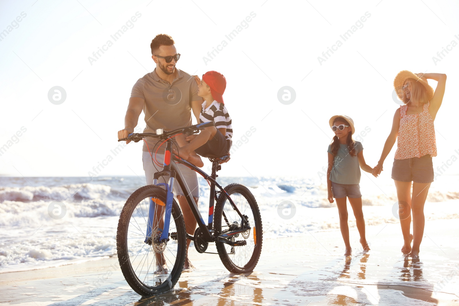 Photo of Happy family with bicycle on sandy beach near sea