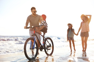 Happy family with bicycle on sandy beach near sea