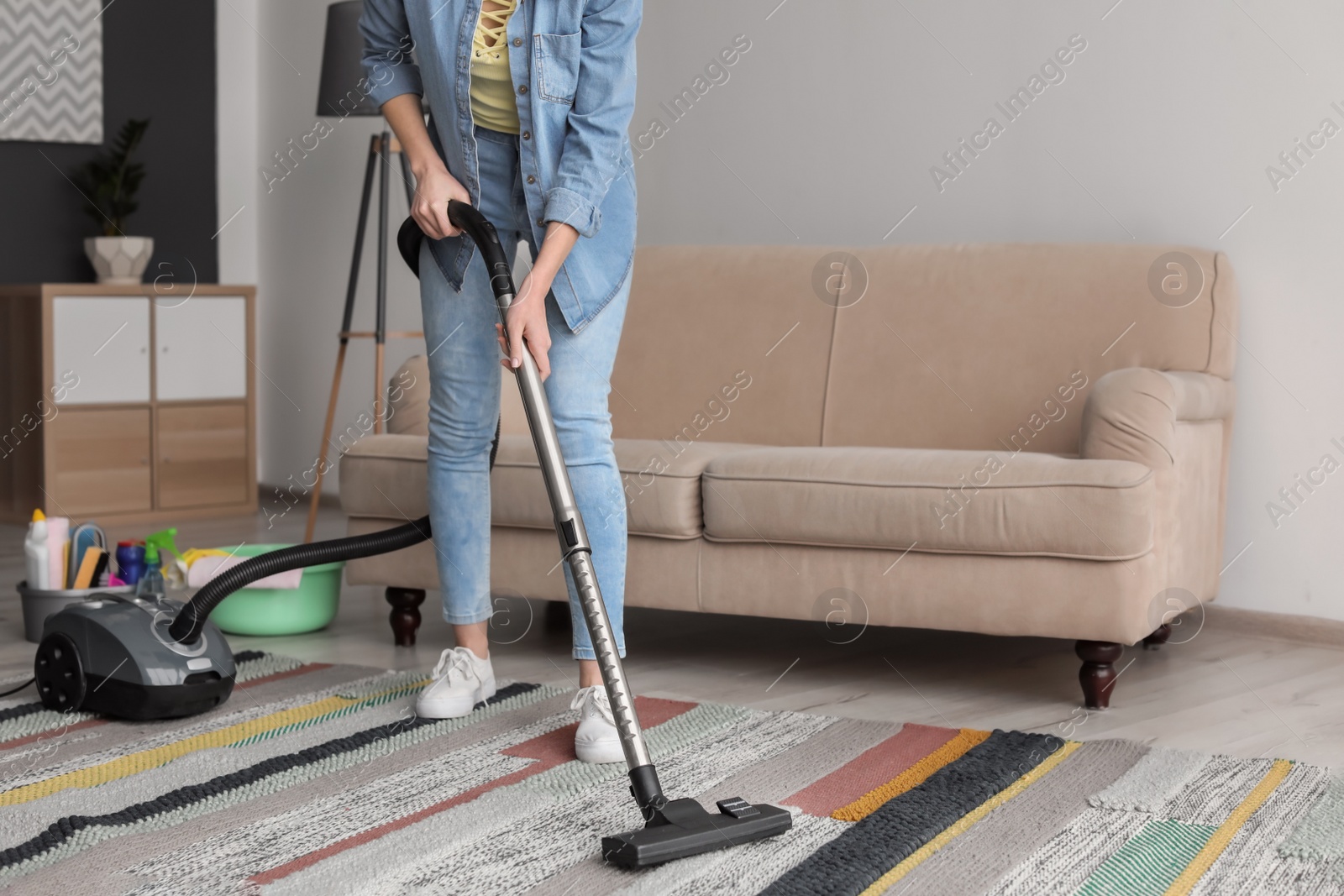 Photo of Young woman hoovering carpet at home