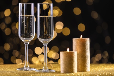 Champagne glasses and golden candles on table against defocused lights. Space for text