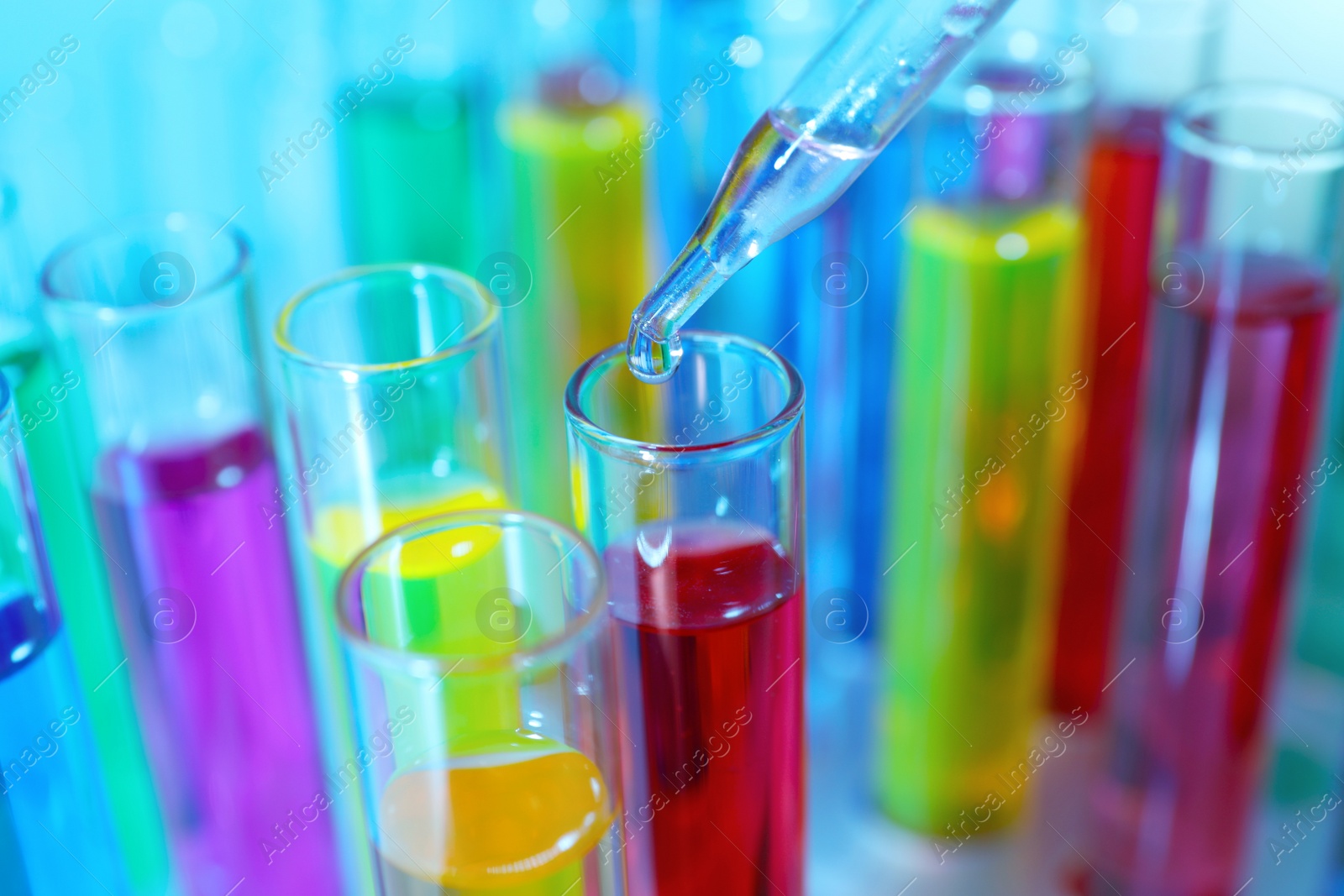 Photo of Dripping liquid from pipette into test tube on light blue background, closeup