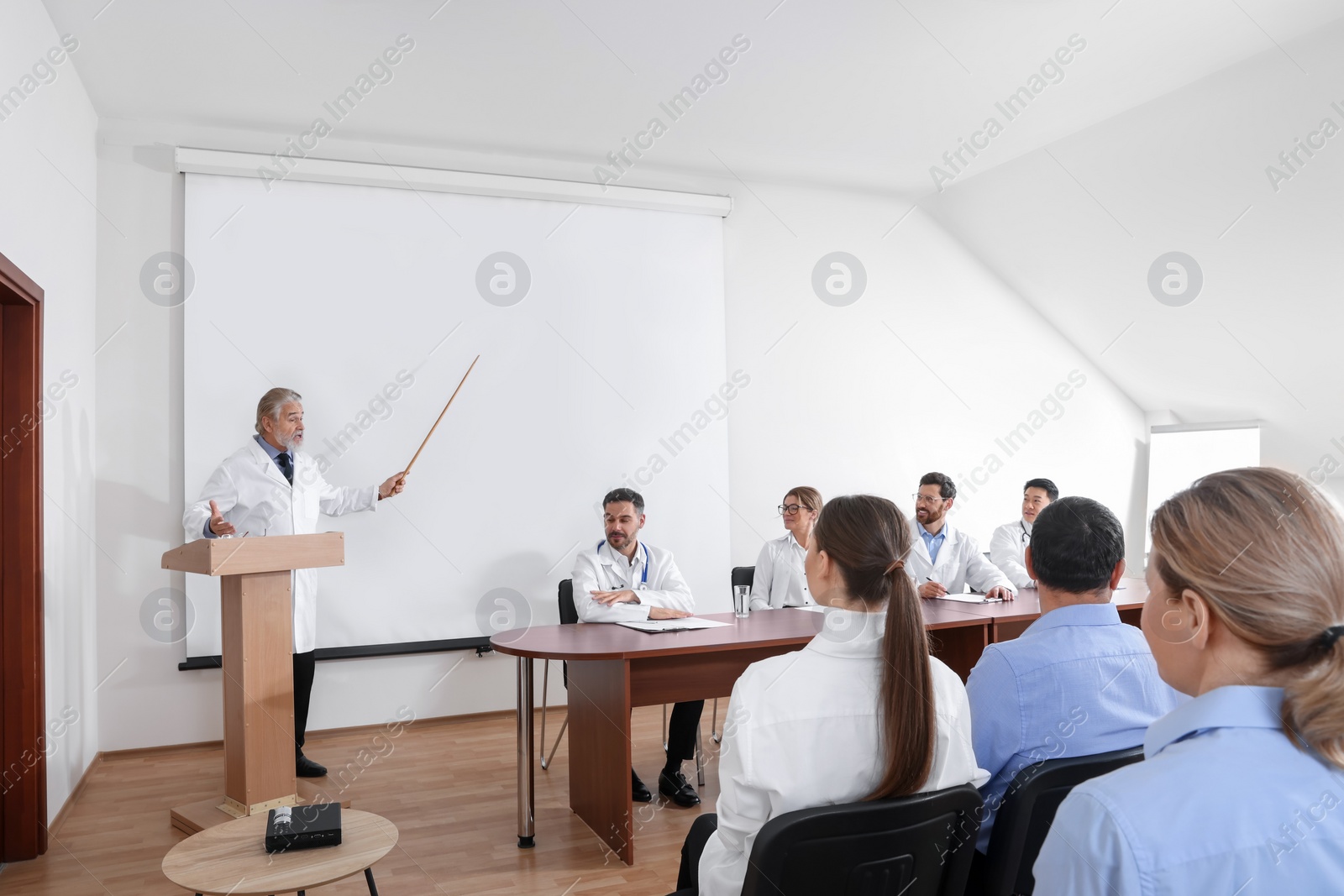 Photo of Senior doctor giving lecture in conference room with projection screen