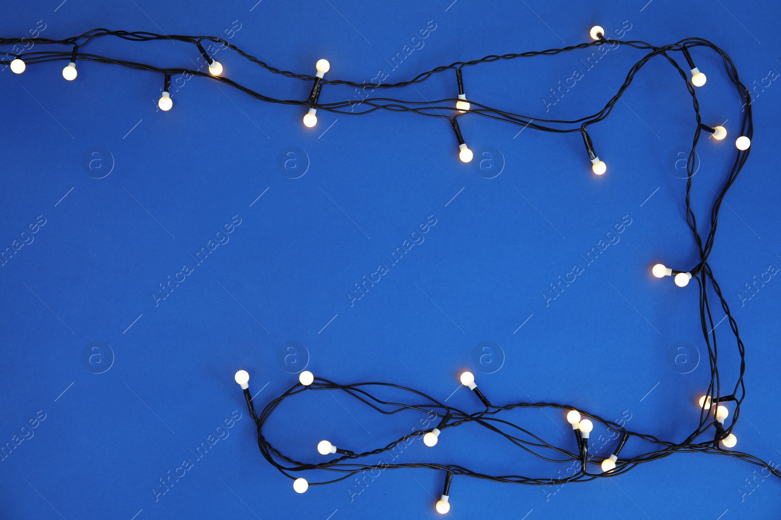 Photo of Glowing Christmas lights on color background, top view