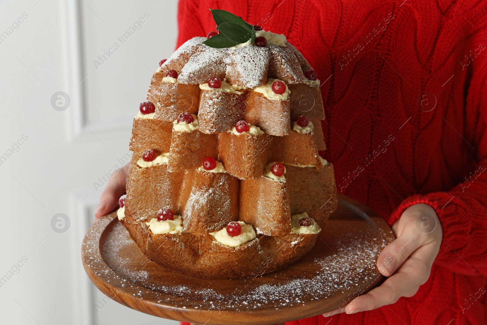 Photo of Woman holding delicious Pandoro Christmas tree cake decorated with powdered sugar and berries indoors, closeup