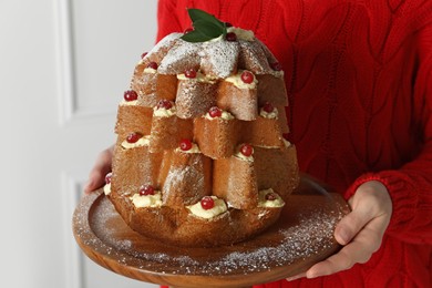 Photo of Woman holding delicious Pandoro Christmas tree cake decorated with powdered sugar and berries indoors, closeup