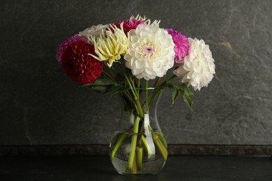 Bouquet of beautiful Dahlia flowers in vase on black table near grey wall