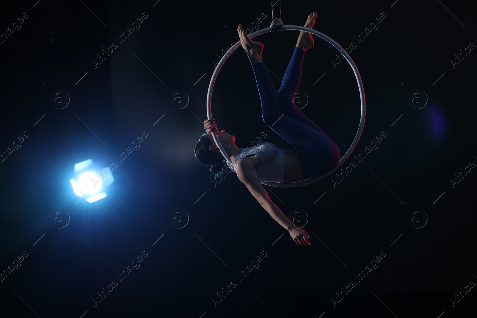 Photo of Young woman performing acrobatic element on aerial ring against dark background. Space for text