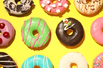 Different delicious glazed doughnuts on yellow background, flat lay