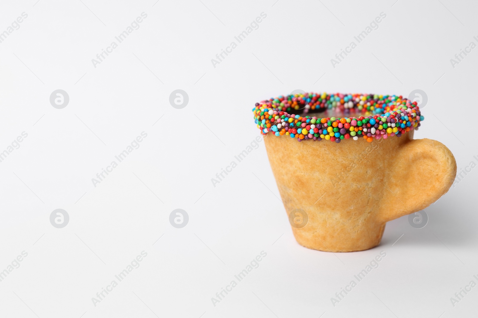 Photo of Delicious edible biscuit coffee cup decorated with sprinkles on white background, space for text
