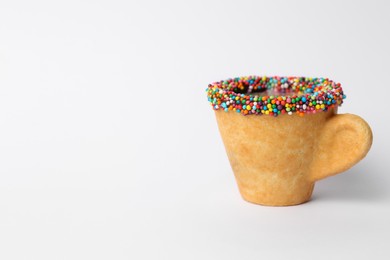 Delicious edible biscuit coffee cup decorated with sprinkles on white background, space for text