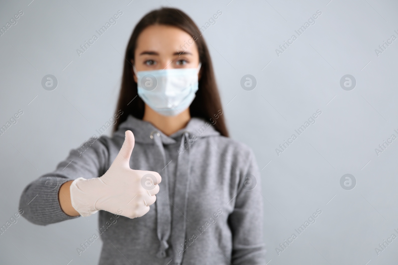 Photo of Woman in protective face mask and medical gloves showing thumb up gesture on grey background. Space for text