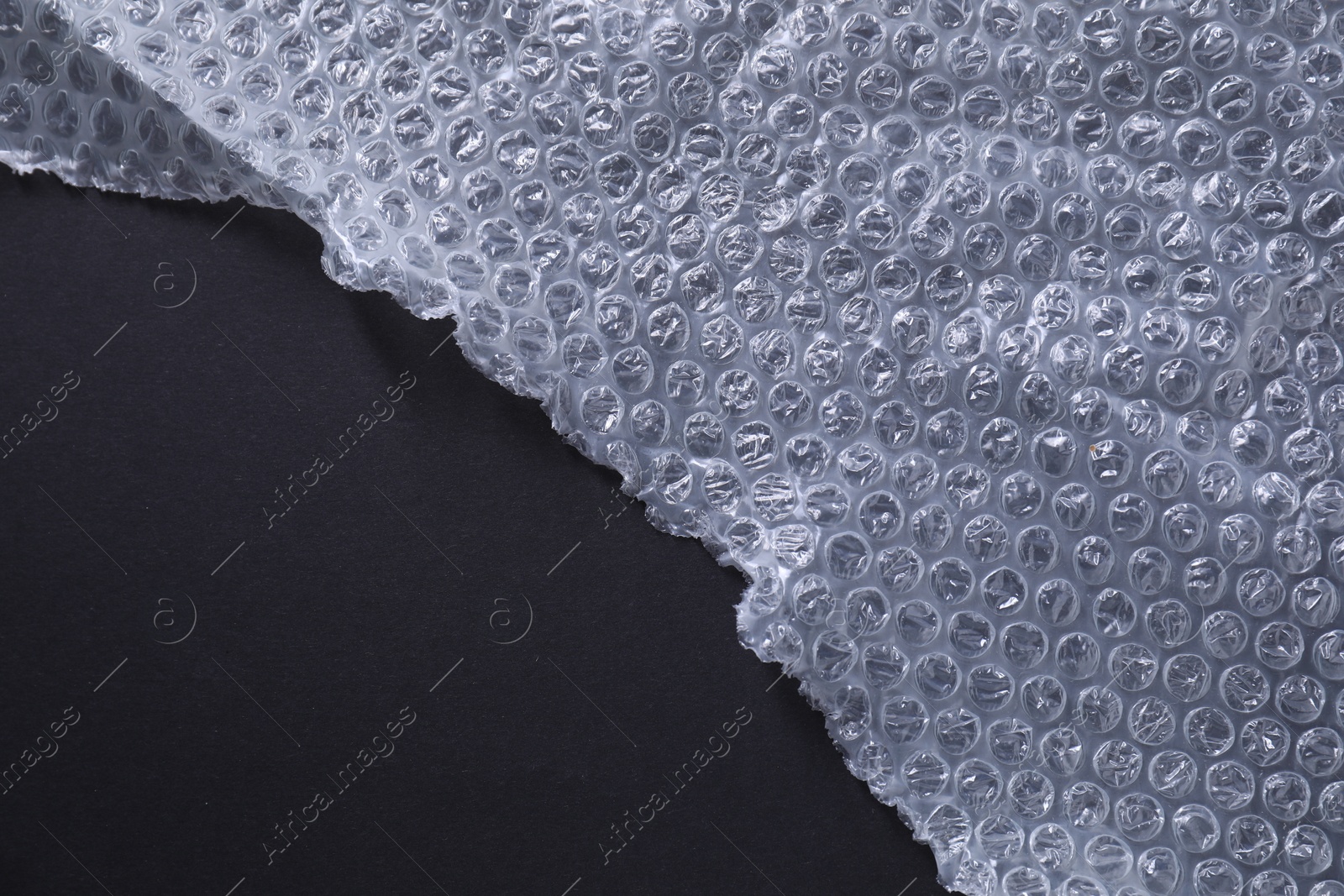 Photo of Transparent bubble wrap on black background, top view. Space for text