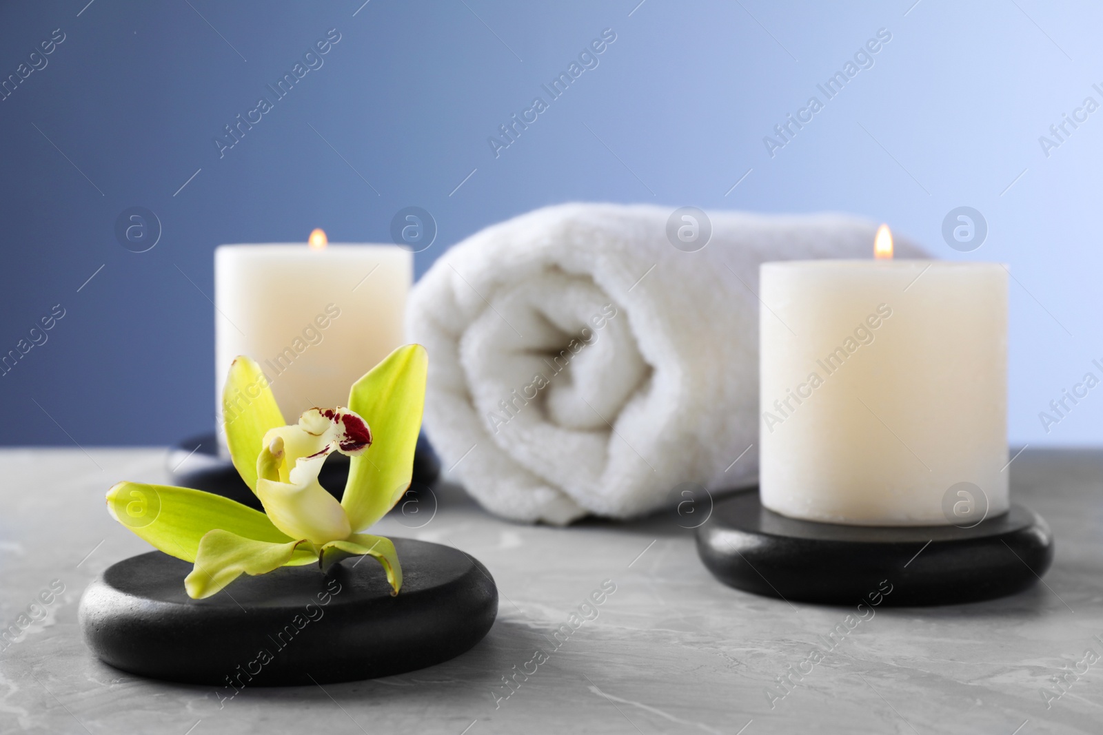 Photo of Spa stones with exotic flower and burning candles on grey table, space for text