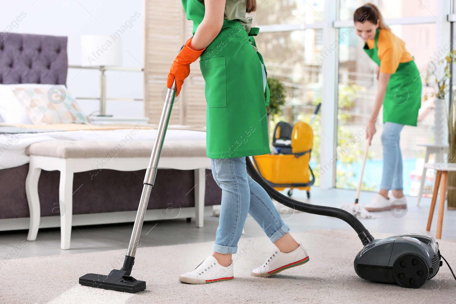 Photo of Woman removing dirt from carpet with vacuum cleaner in bedroom