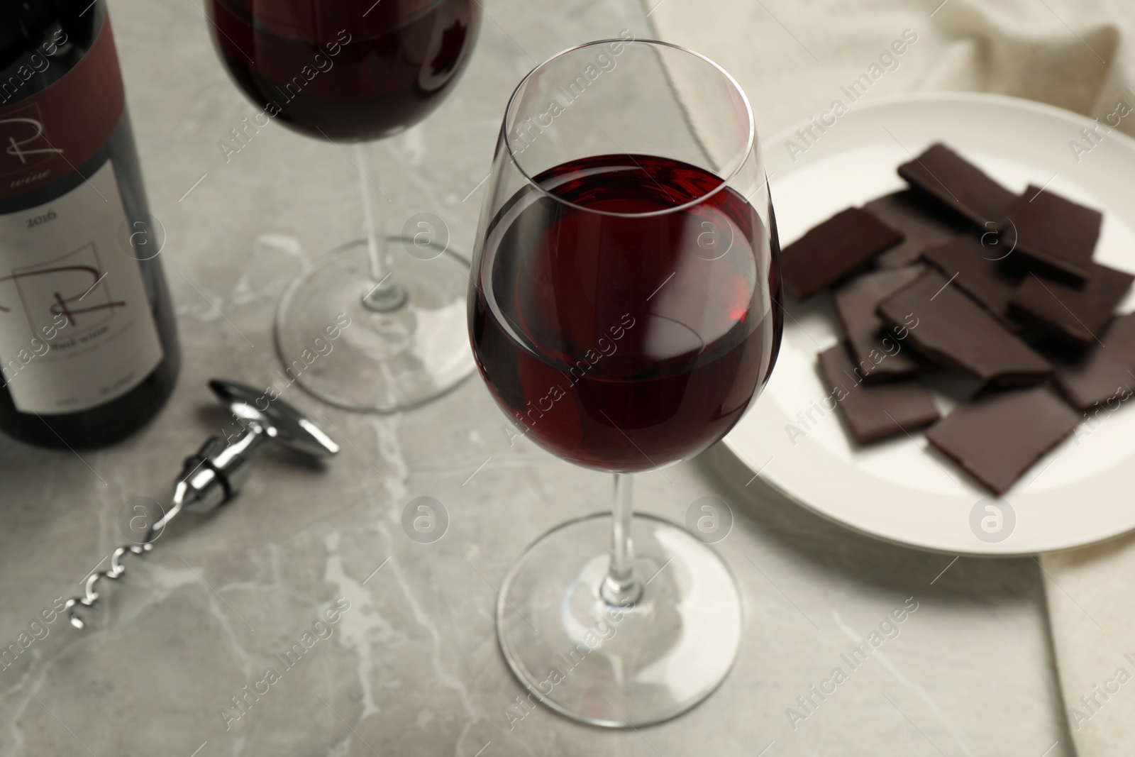 Photo of Glass of red wine with chocolate on light marble table