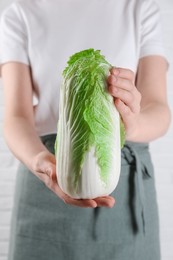 Photo of Woman holding fresh Chinese cabbage near white wall, closeup