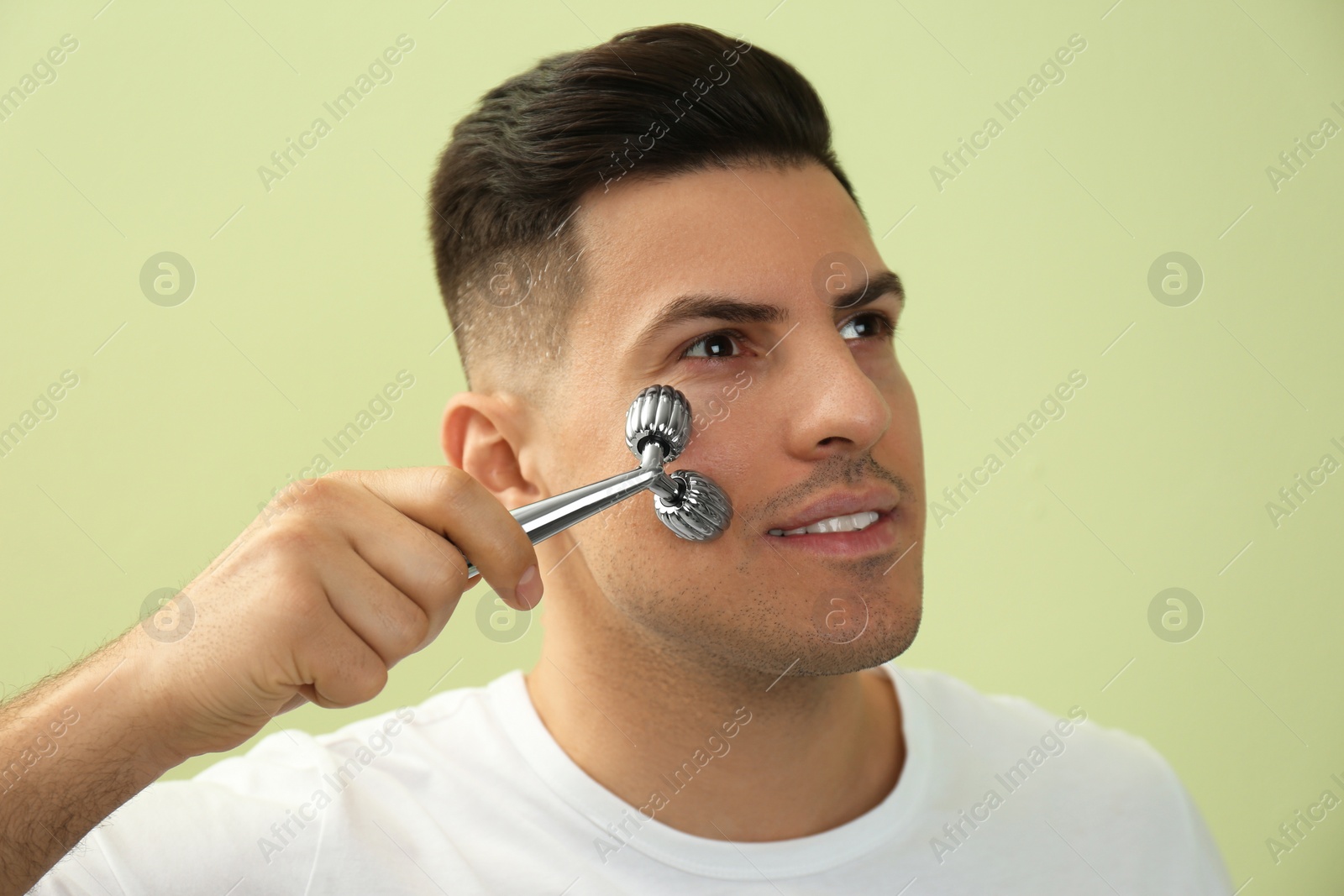 Photo of Man using metal facial roller on green background