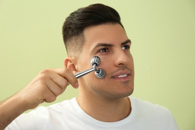 Man using metal facial roller on green background