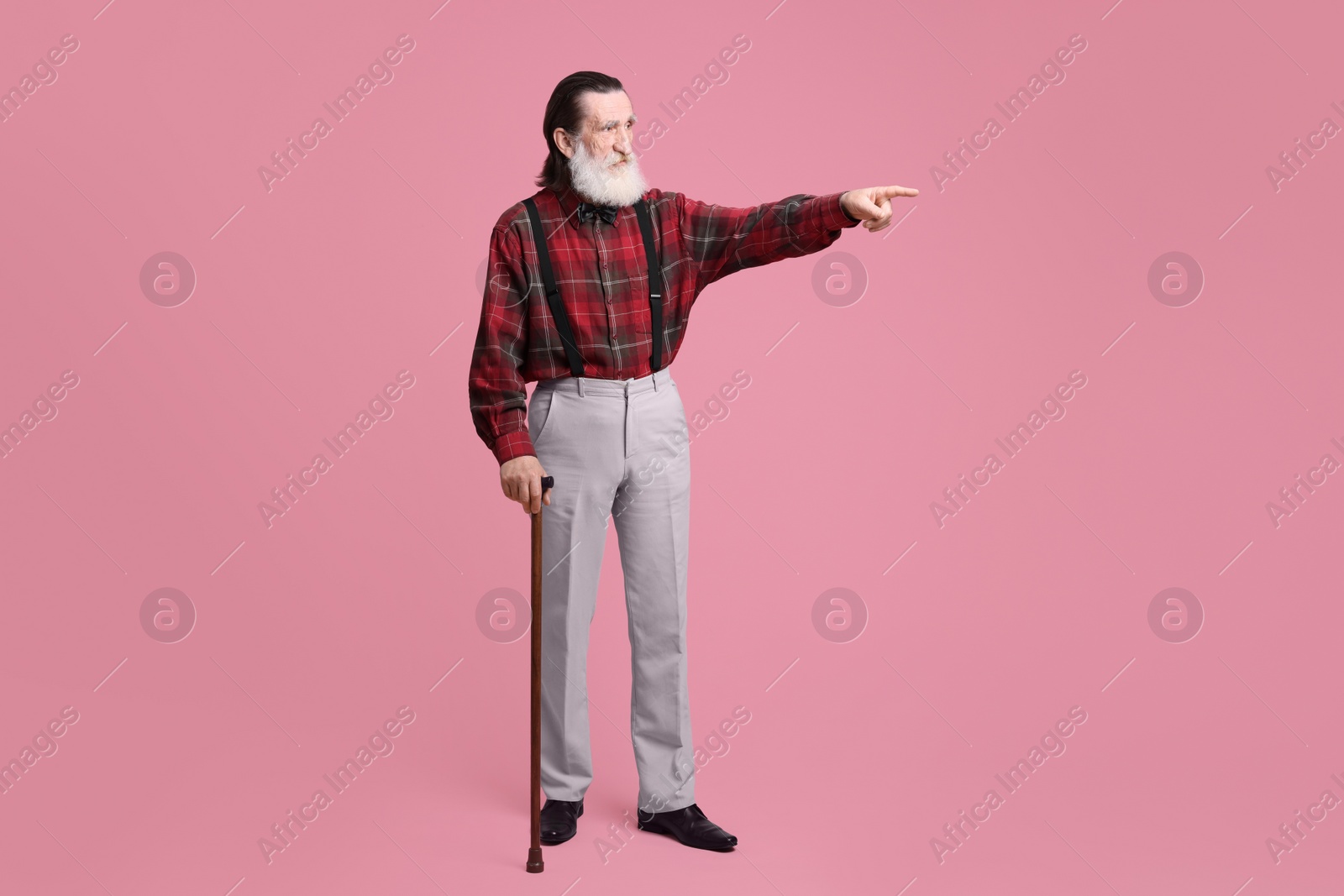 Photo of Senior man with walking cane pointing at something on pink background
