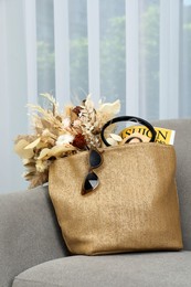 Stylish beach bag with beautiful bouquet of dried flowers, sunglasses and magazine on sofa in room