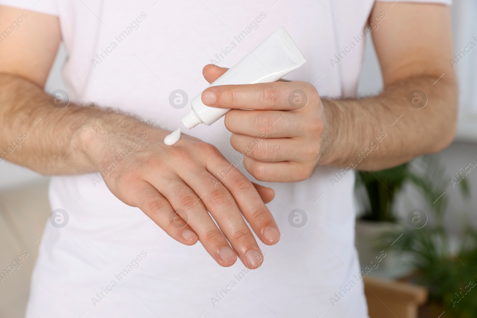 Photo of Man applying cream onto hand at home, closeup