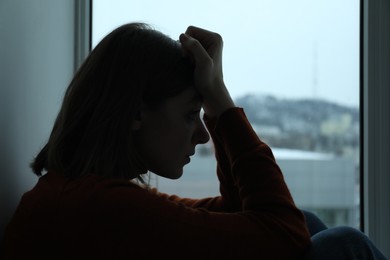 Sad young woman near window at home