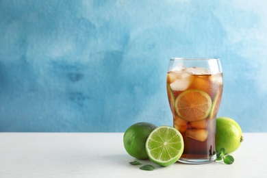 Glass of coke with ice cubes and limes on table against color background. Space for text