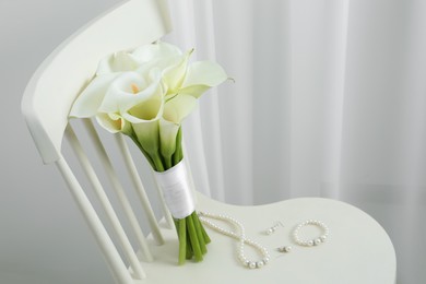 Beautiful calla lily flowers tied with ribbon and jewelry on white chair indoors