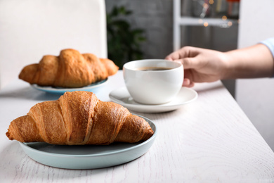 Photo of Tasty fresh croissants and woman with coffee at white wooden table, closeup