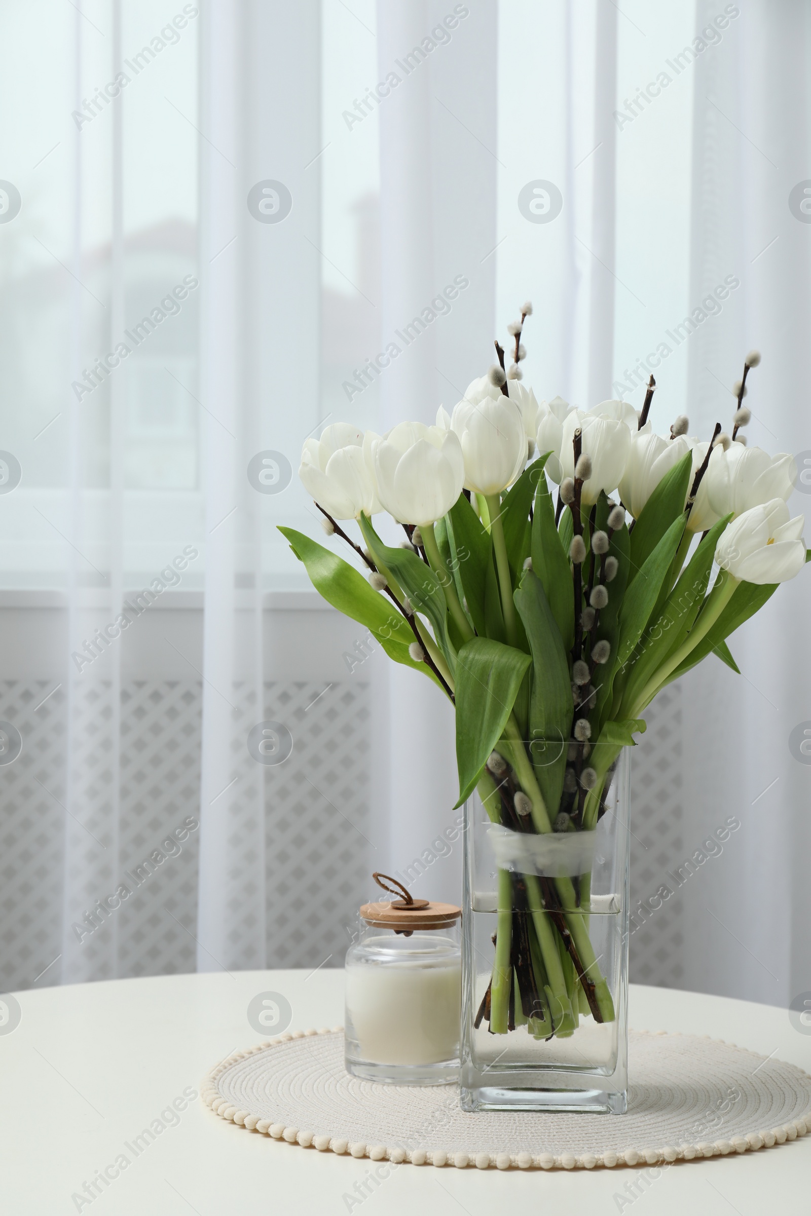 Photo of Beautiful bouquet of willow branches and tulips in vase on table indoors, space for text