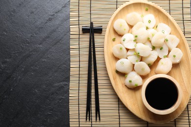 Photo of Raw scallops with green onion, soy sauce and chopsticks on dark textured table, top view
