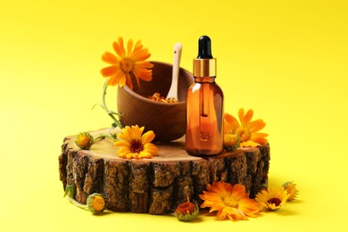 Mortar with pestle, bottle of essential oil and beautiful calendula flowers on yellow background