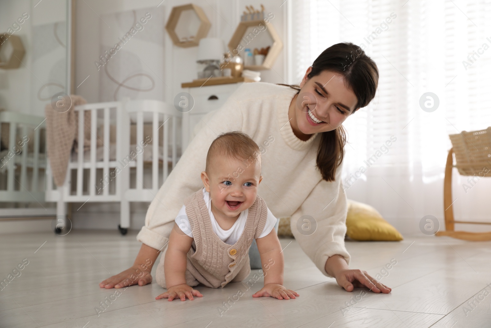 Photo of Happy young mother watching her cute baby crawl on floor at home