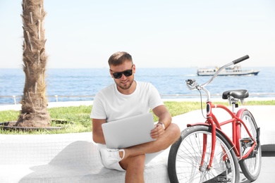 Attractive man with laptop and bike near sea