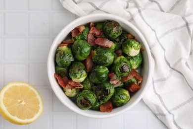 Photo of Delicious roasted Brussels sprouts, bacon and lemon on white tiled table, top view