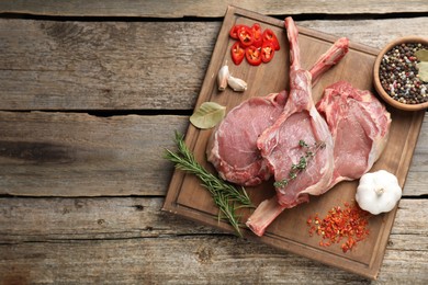 Photo of Fresh tomahawk beef cuts and spices on wooden table, top view. Space for text