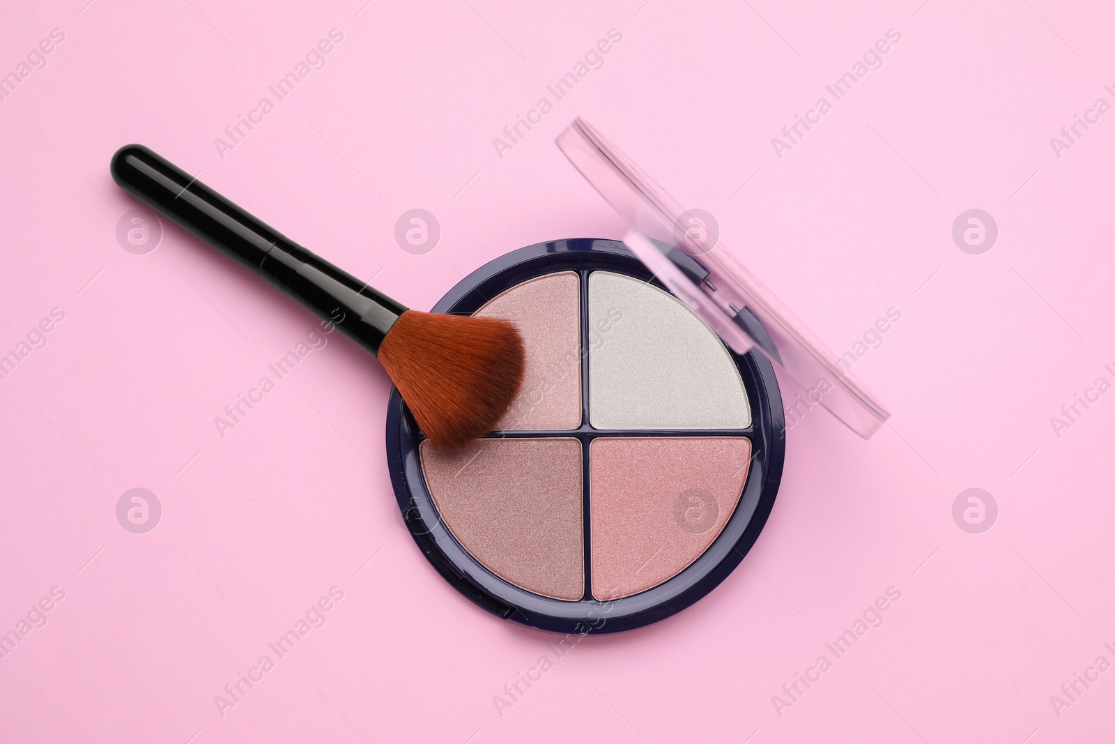 Photo of Colorful contouring palette with brush on pale pink background, top view. Professional cosmetic product