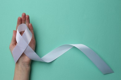 Photo of Woman holding white awareness ribbon on turquoise background, top view. Space for text