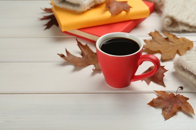 Cup of hot coffee, books and autumn leaves on white wooden table, space for text