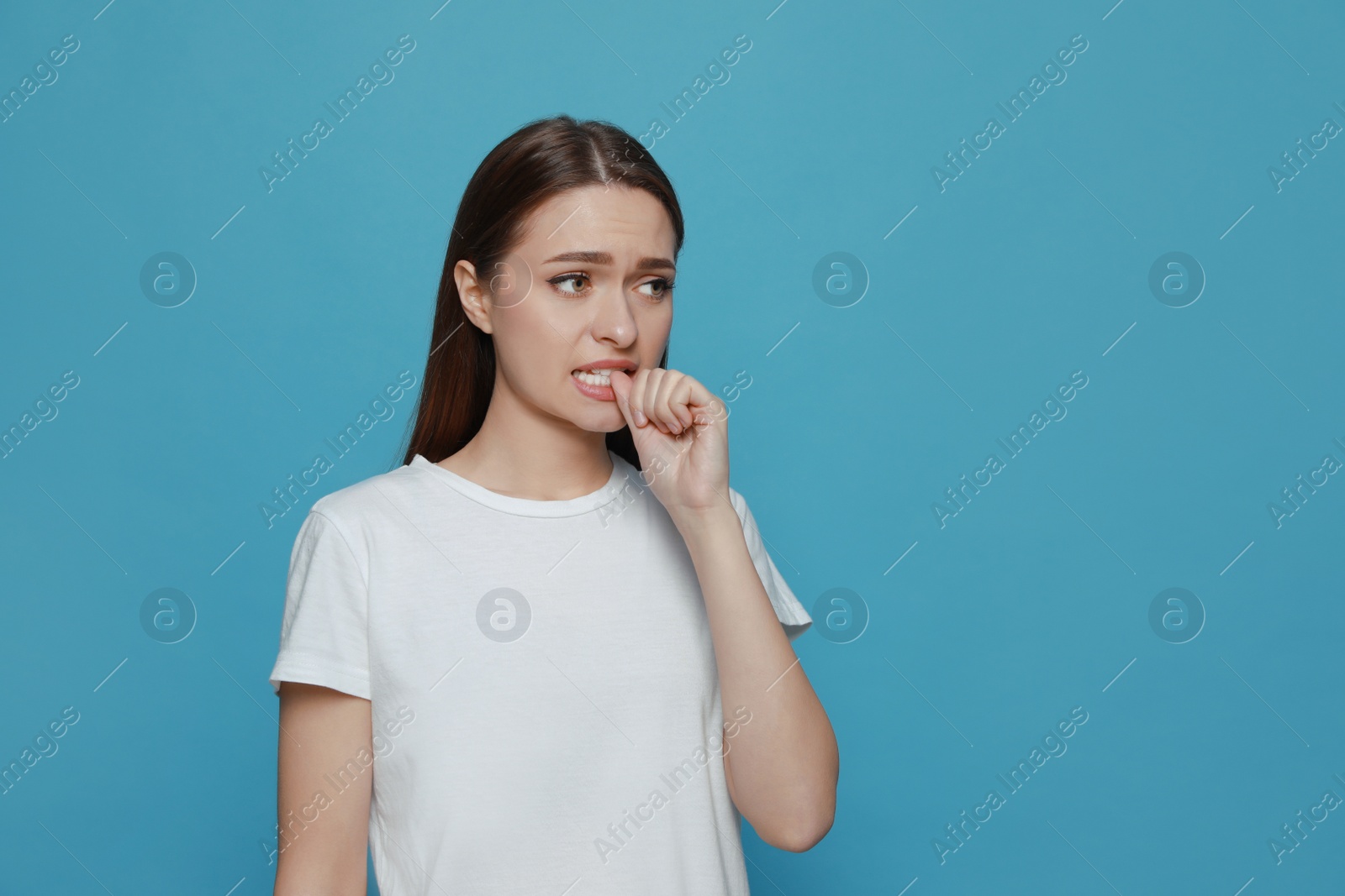 Photo of Young woman biting her nails on light blue background. Space for text