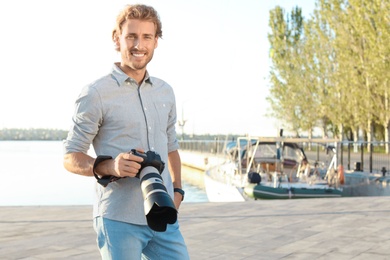 Handsome male photographer holding professional camera at pier. Space for text