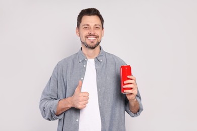 Photo of Happy man holding red tin can with beverage and showing thumb up on light grey background