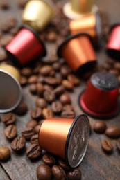 Many coffee capsules and beans on wooden table, closeup