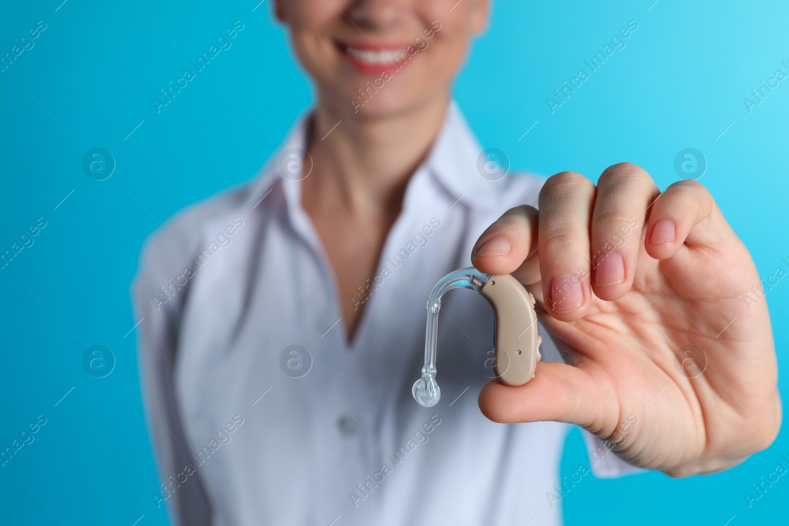 Photo of Female doctor holding hearing aid on color background, closeup. Medical object