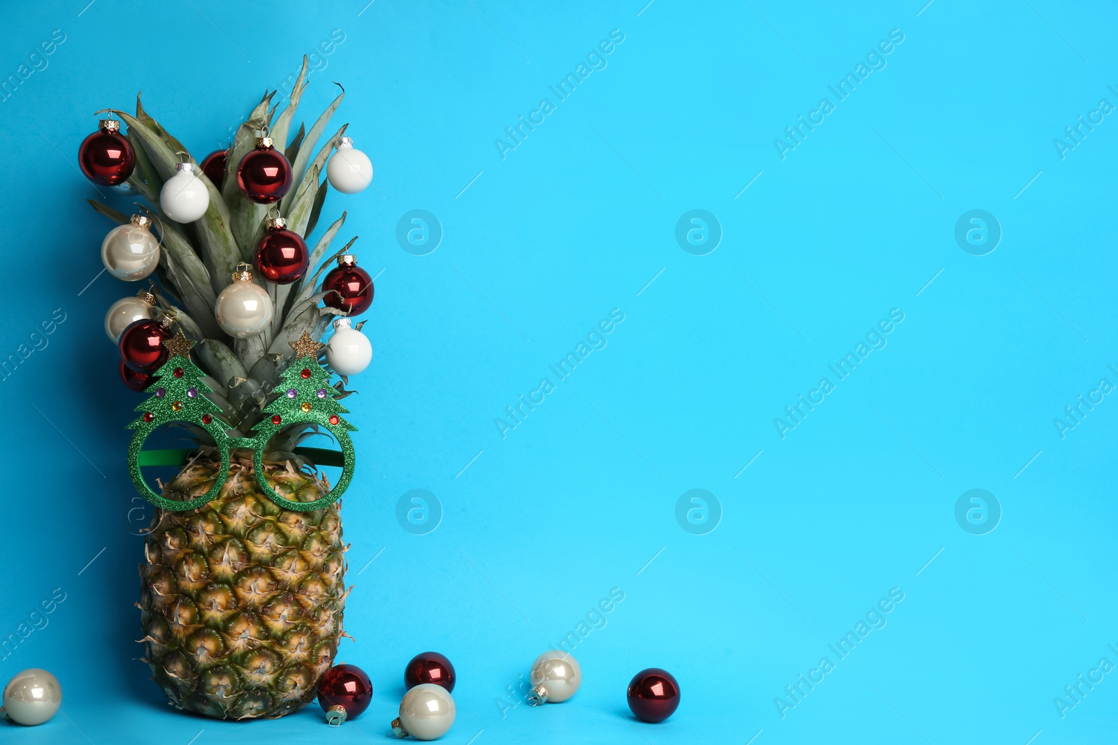 Photo of Pineapple with party glasses and Christmas tree balls on light blue background, space for text. Creative concept