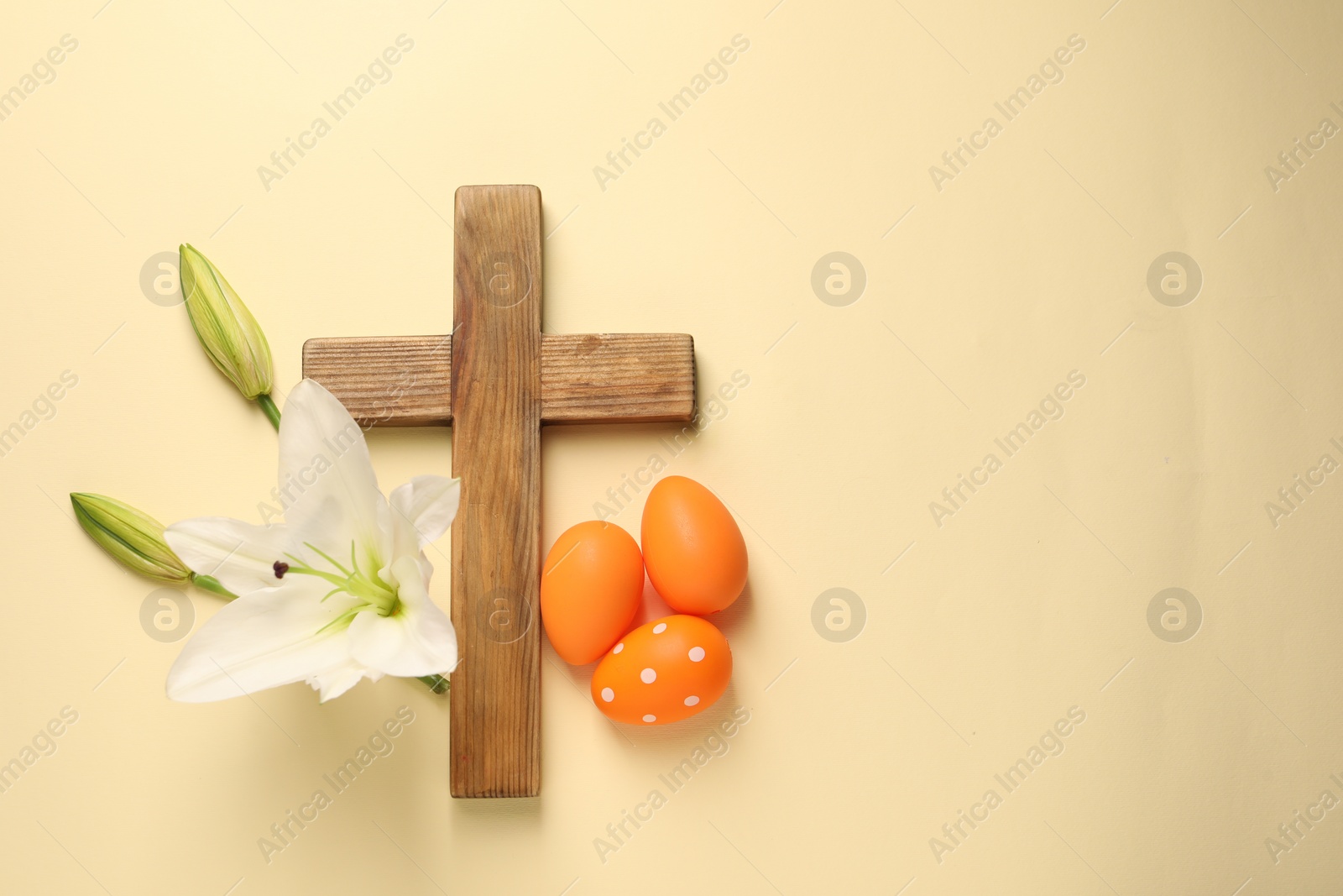 Photo of Wooden cross, painted Easter eggs and lily flowers on pale yellow background, flat lay. Space for text