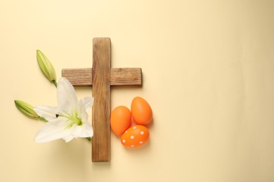 Photo of Wooden cross, painted Easter eggs and lily flowers on pale yellow background, flat lay. Space for text