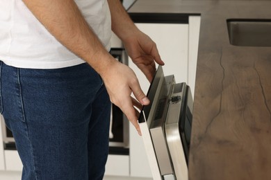 Man opening dishwasher's door in kitchen, closeup