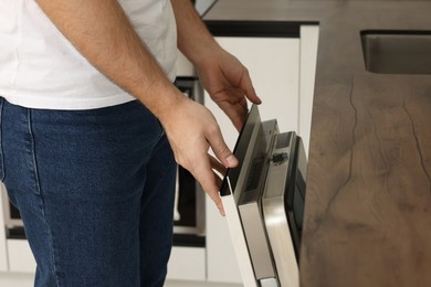 Photo of Man opening dishwasher's door in kitchen, closeup