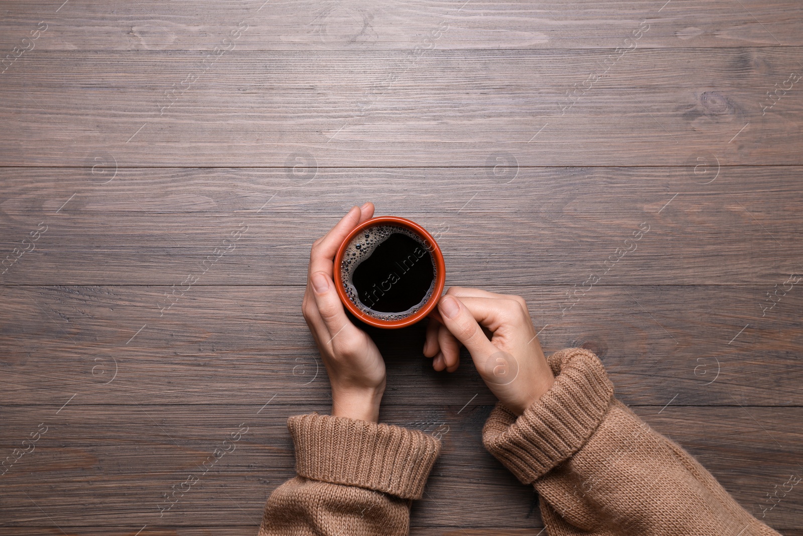 Photo of Woman with cup of coffee at wooden table, top view. Space for text